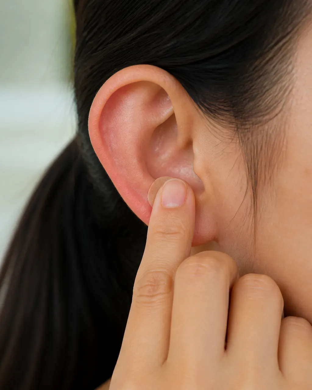 Fingertip pressing an ear seed plaster until the point feels warm