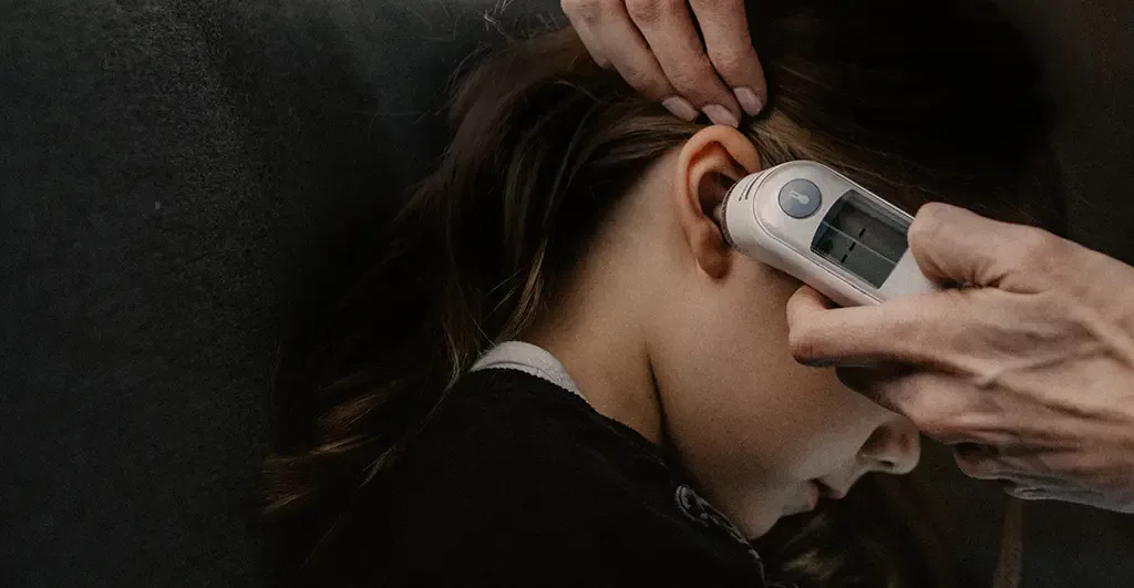 Adult hands using a digital ear thermometer to check a child's temperature during a feverish illness