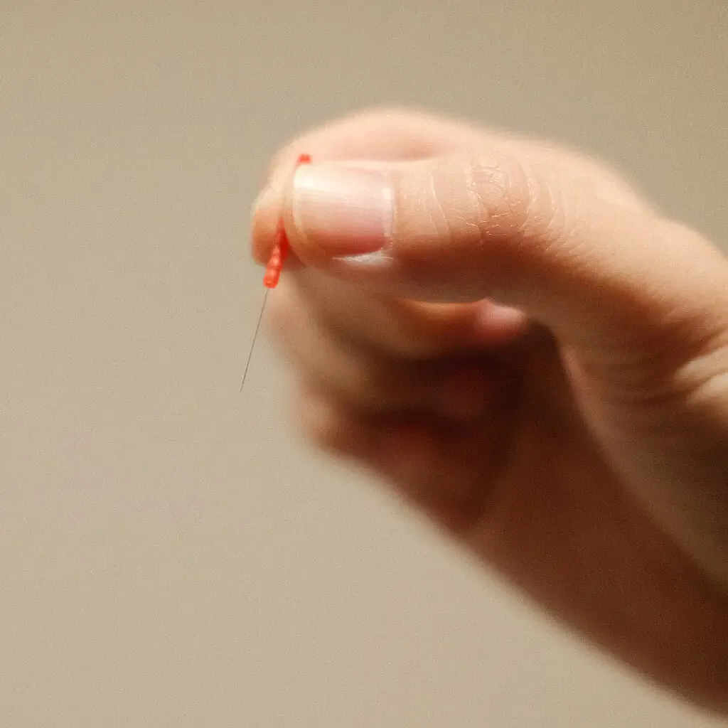 Close-up of a colour-coded Seirin acupuncture needle held between fingertips